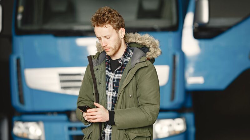 Operador revisando la ubicación GPS de las unidades en su teléfono frente a la flota de tractocamiones